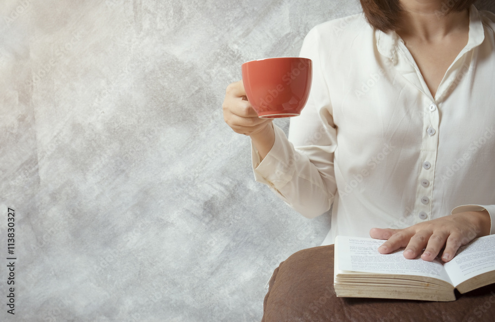 A Girl reading a book on pillow and drinking coffee.