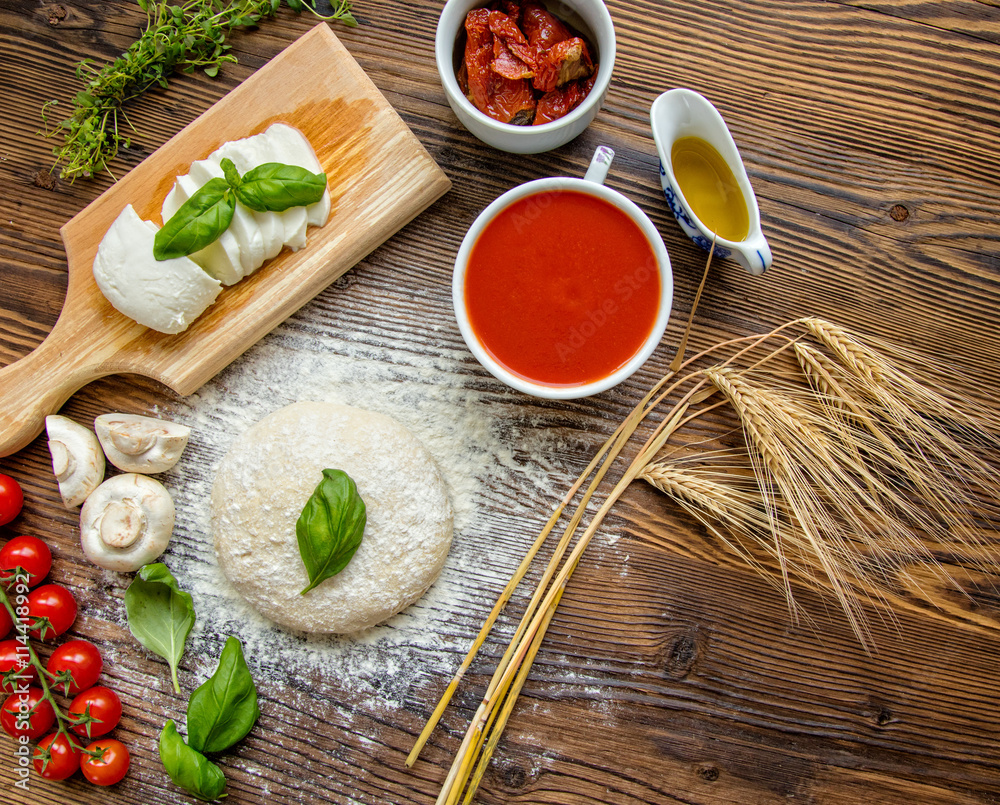 Pizza dough with tomato sauce on wooden table