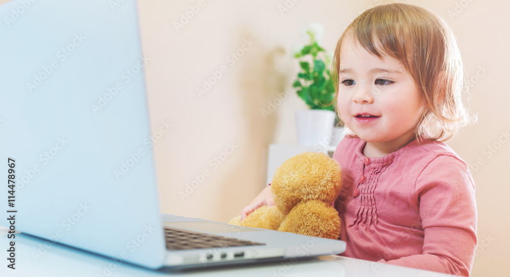 Toddler girl using a laptop with her teddy bear