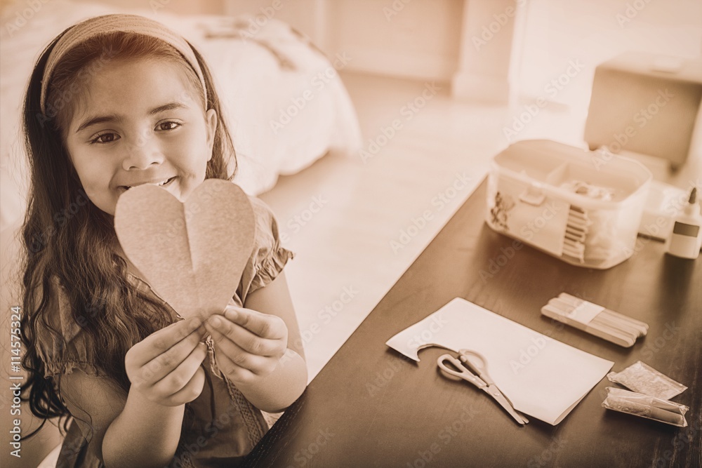 Cute young girl holding heartshape paper at table