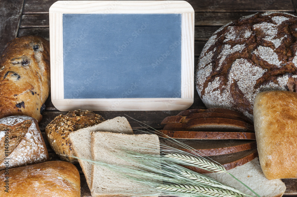 Verschiedene Brotsorten mit einer Tafel auf einem Holztisch / Brotsorten mit Getreideaehren und eine