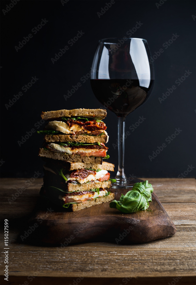 Caprese sandwich or panini and glass of red wine. Whole grain bread, mozzarella, dried tomatoes, bas