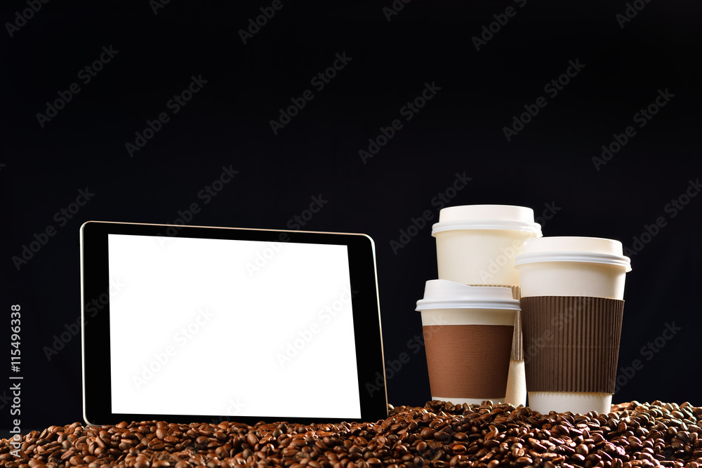 Tablet computer with blank white screen and paper cups of coffee on pile of coffee beans

