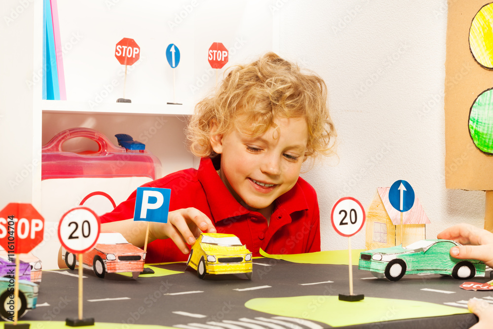 Cute boy playing driver with toy paper cars