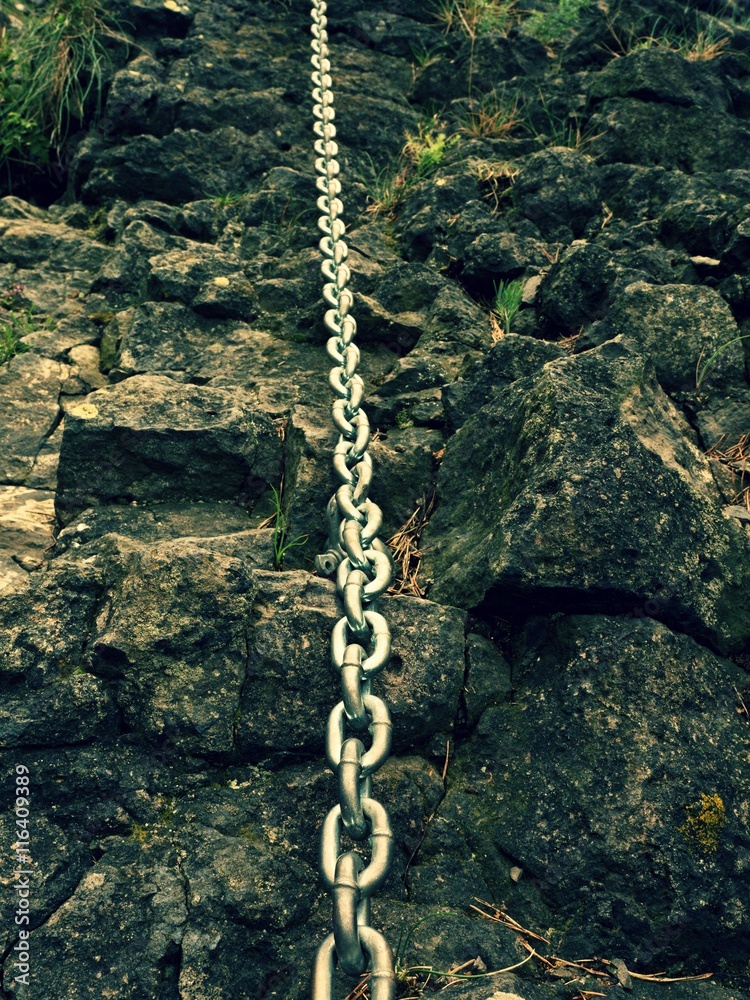 Detail of chain anchored in hard whinstone rock. Climbers path