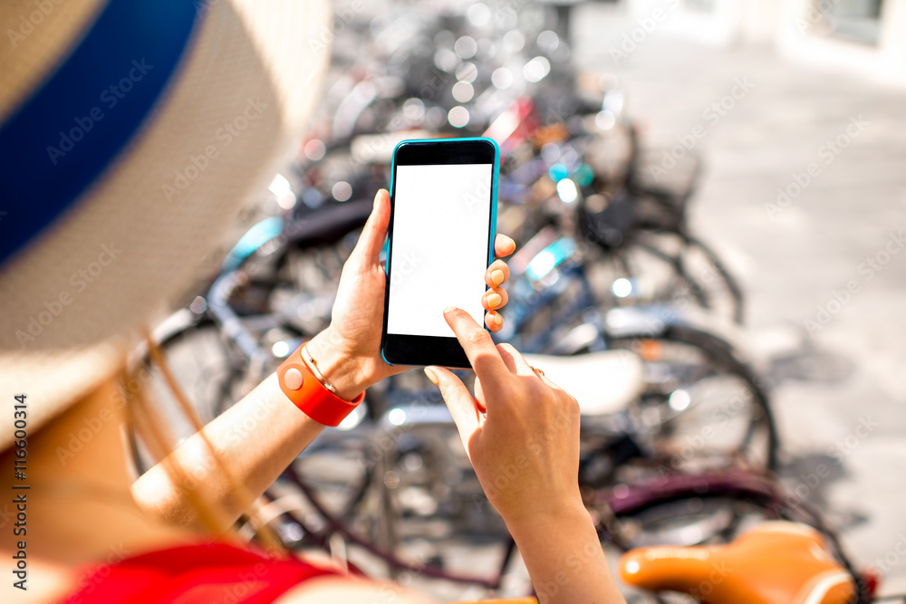 Woman holding smart phone with white screen on the bicycle parking background. Bicycle rent with sma