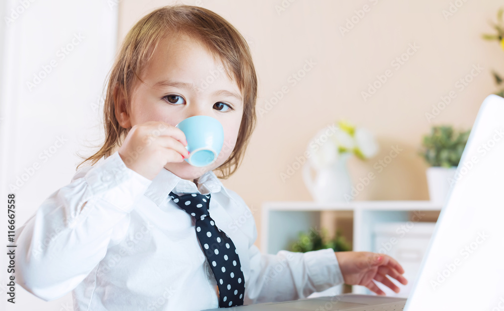 Toddler girl drinking from a mug in front of a laptop