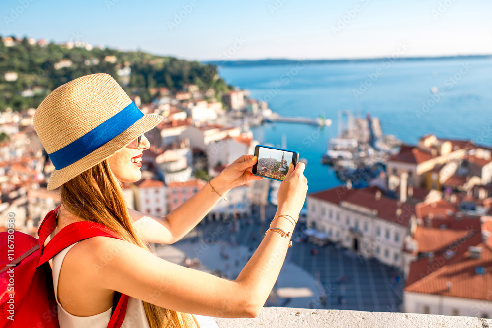 Young female traveler with red backpack and photo camera enjoying the view on Piran old town. Travel