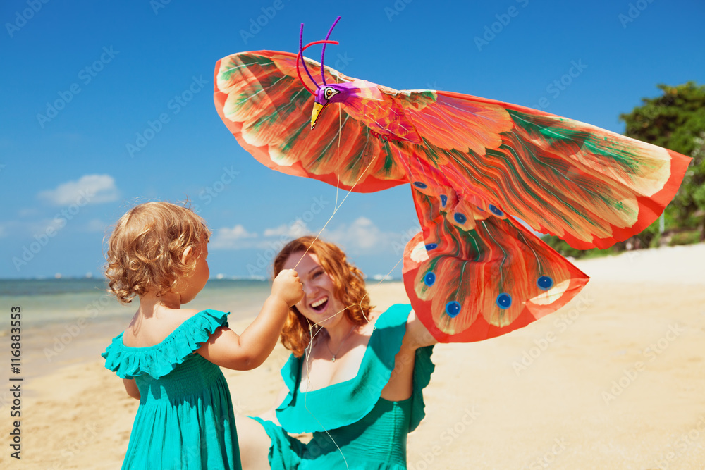 Happy family has fun on sunny sand beach - mother and baby girl walk together along ocean surf and l