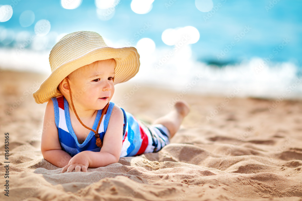 little boy lying the beach in straw hat