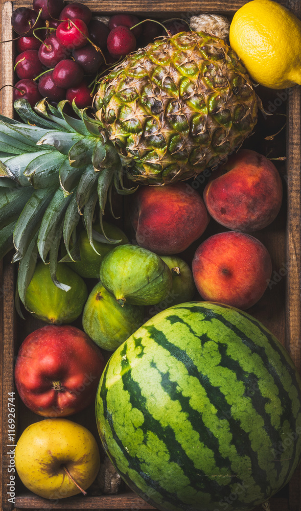 Summer friut variety in wooden tray over wooden background, top view. Watermelon, pineapple, lemon, 