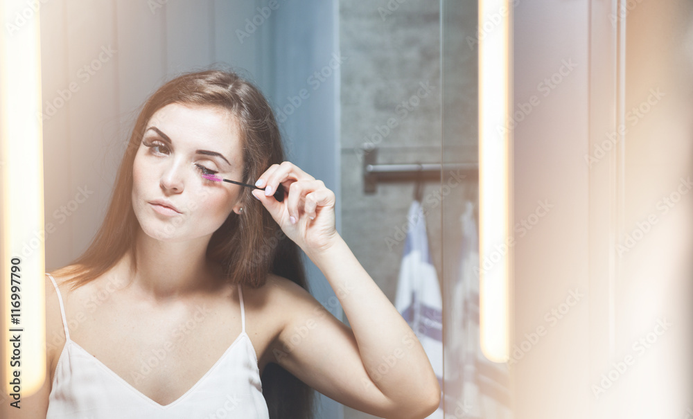 Woman applying mascara on long eyelashes in front of mirror