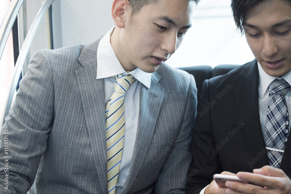 Two businessmen looking at a smart phone on a train