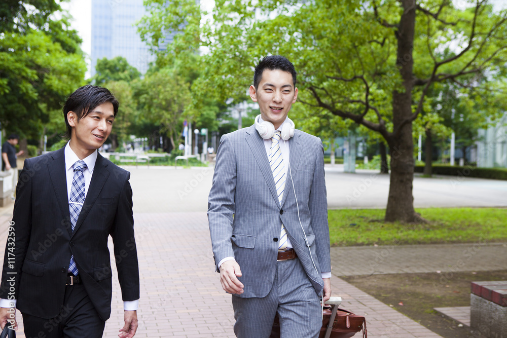 Two young business man is walking in the park while talking