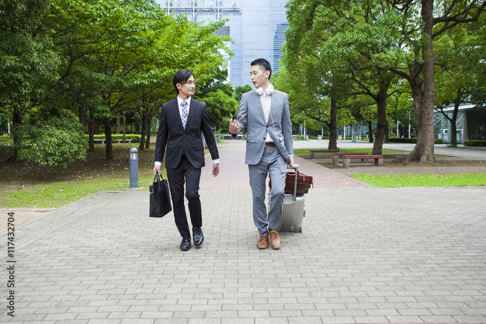 Two young business man is walking in the park while talking