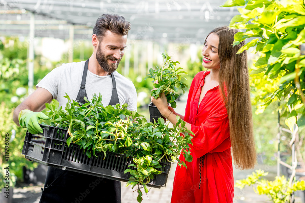 英俊的卖花人站在植物店里帮助女买家选花。顾客