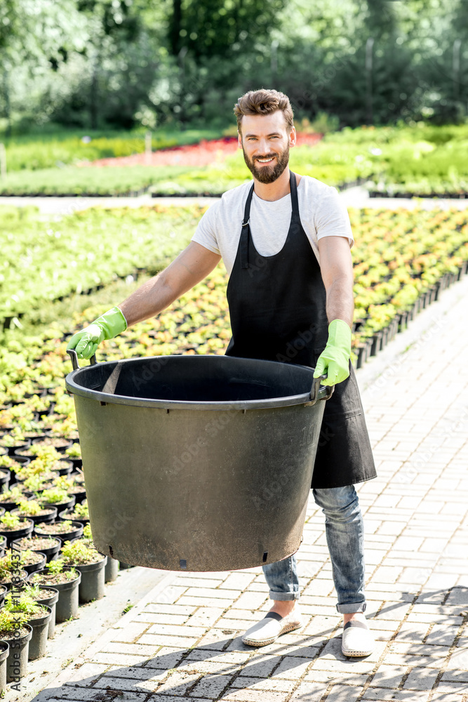 Handsome gardener holding huge bucket for growing trees on the plantation