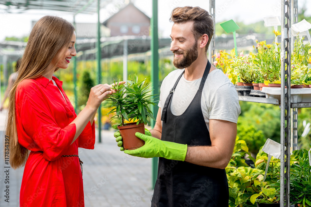 英俊的卖花人站在植物店里帮助女买家选花。顾客