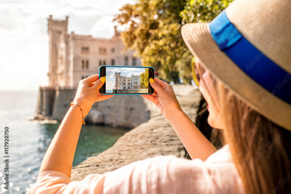 Young woman having fun photographing landscape near Miramare castle in northeastern Italy. Traveling