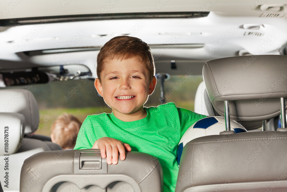 Happy kid boy sitting in the car and holding ball