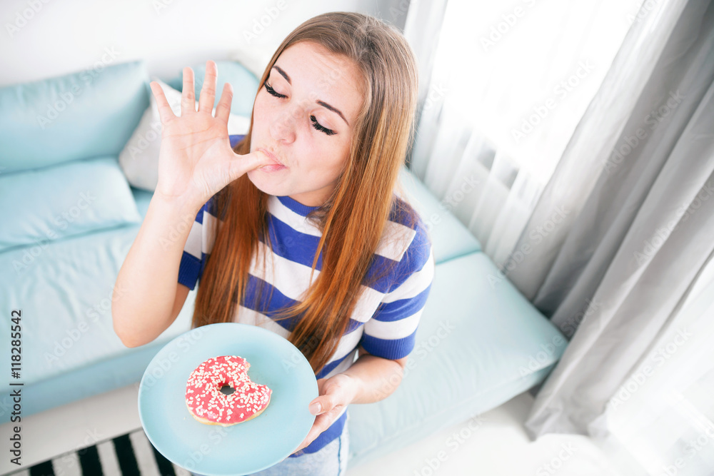 Woman at home eating donut and licking her finger