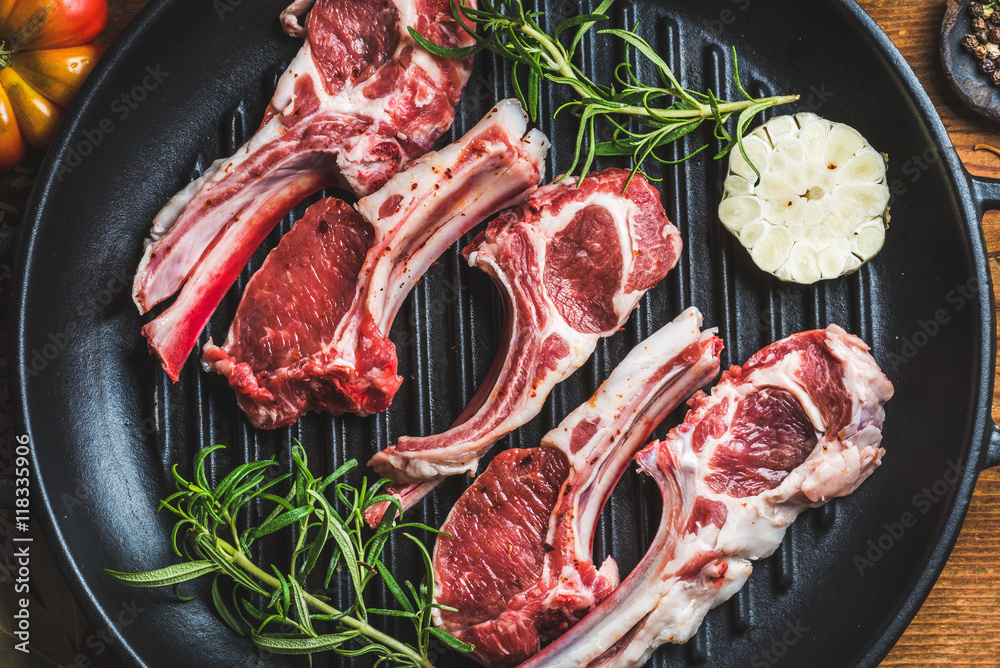 Raw uncooked lamb meat chops with rosemary and garlic in black iron grilling pan, top view, horizont