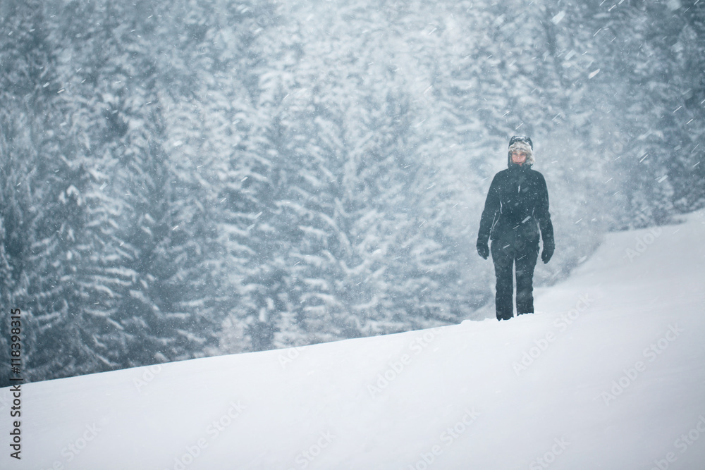 A woman walking on the snow-covered meadow during heavy snowfall.