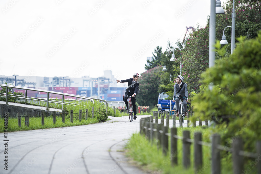 Two businessmen are riding on the road bike in the park wearing a helmet