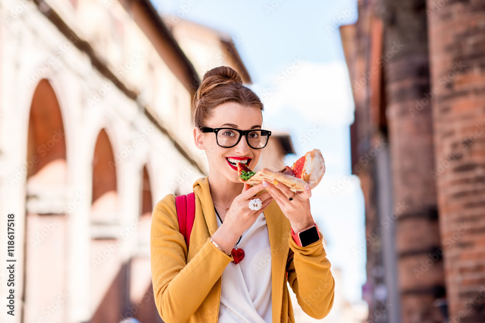 Young female student eating pizza on the break near the university in Bologna city in Italy