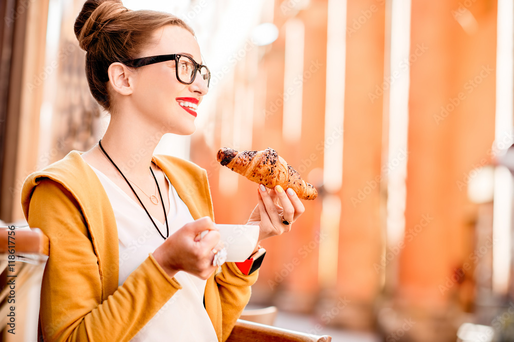 Young woman having italian breakfast with croissant and coffee at the cafe on the street in Bologna 