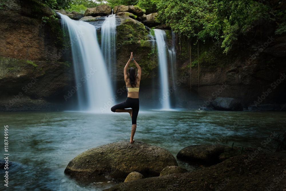 Young woman in a yoga pose at the waterfall, she felt relaxed. T