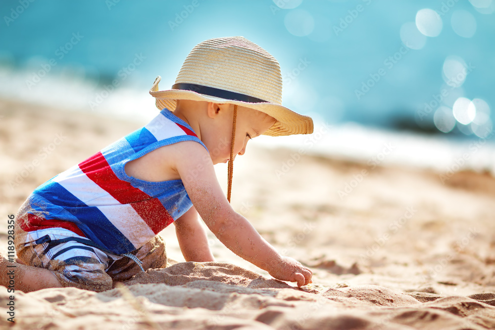 little boy playing at the beach in straw hat