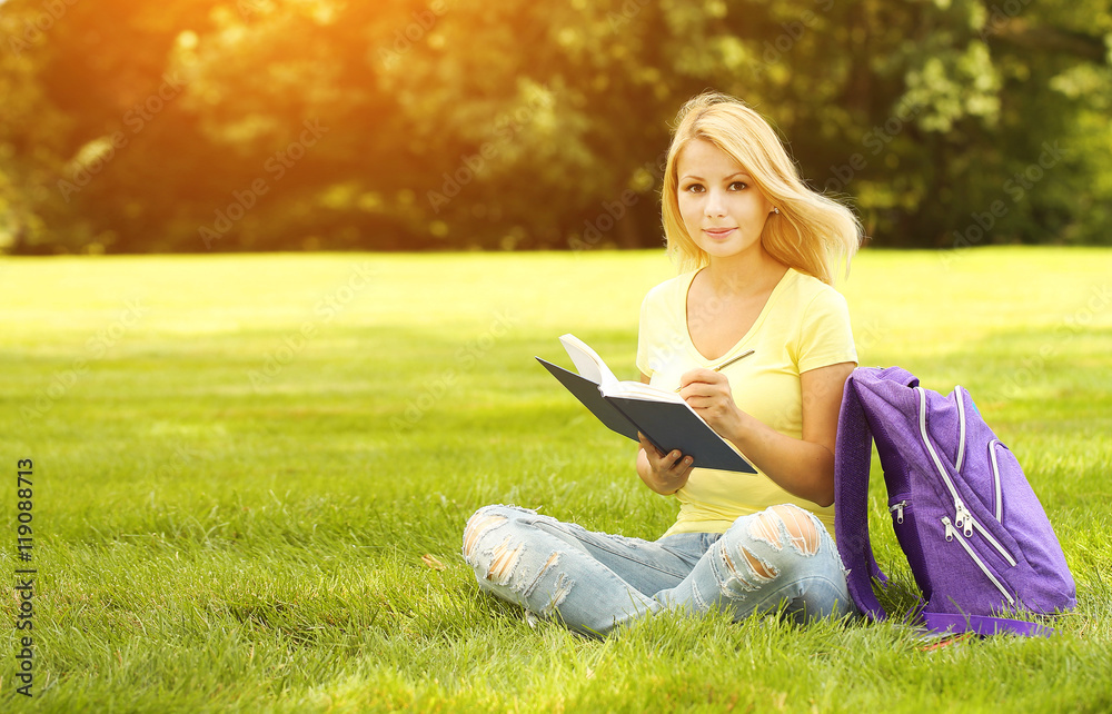 Student girl with book and backpack in park. Blonde young woman.