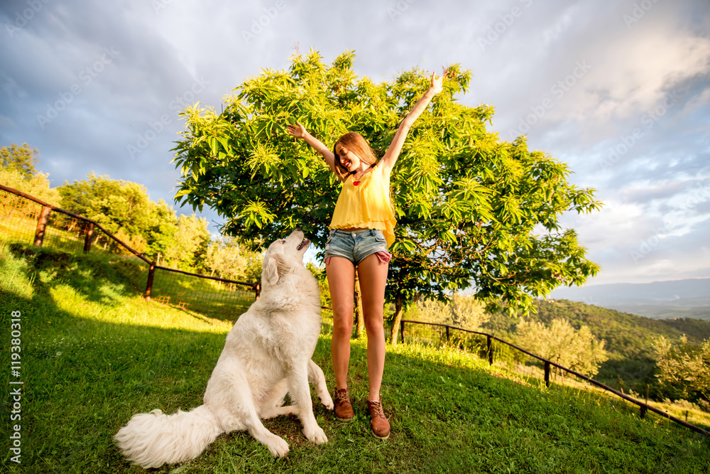 Young and happy woman playing with Maremma italian sheepdog on the lawn in the countryside in Tuscan