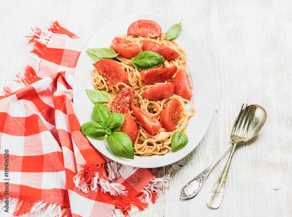 Pasta dinner. Spaghetti with roasted tomatoes and fresh basil in oval dish over white wooden backgro