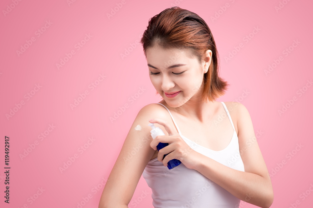 Woman use body lotion on arms and touching her skin on pink back