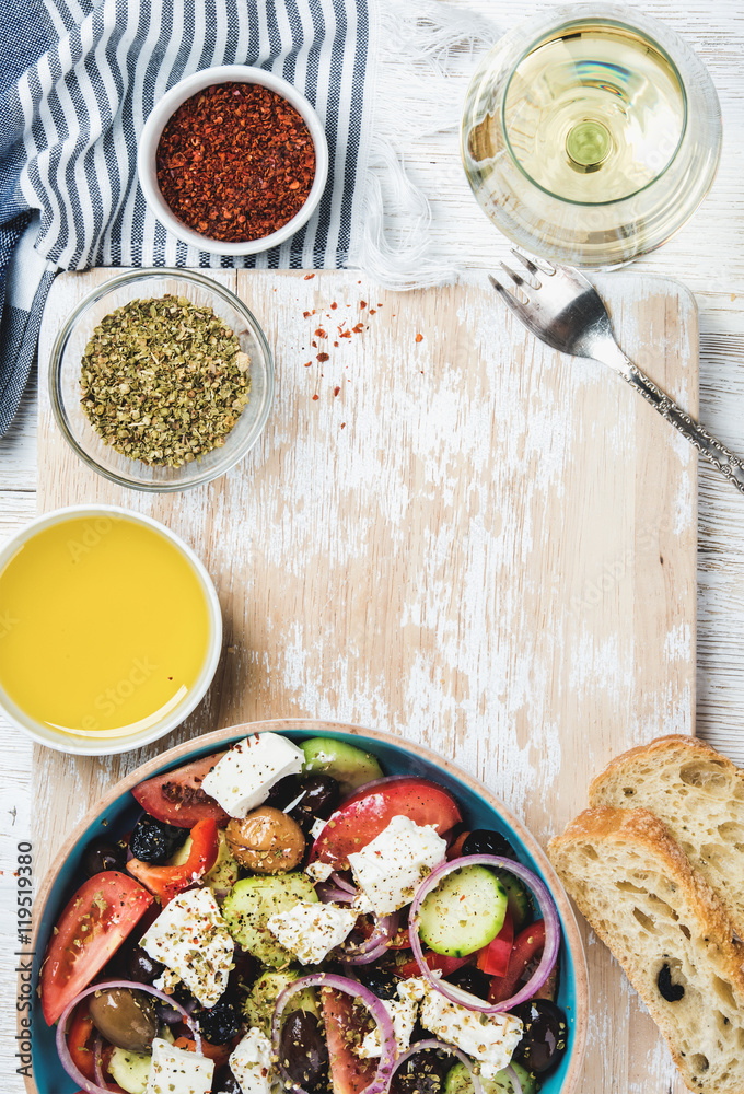 Greek salad with olive oil, bread, oregano, pepper and glass of white wine over old white painted wo