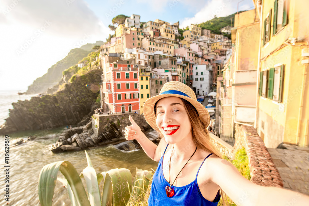 Young female traveler making selfie photo on the old coastal town in Riomaggiore in Italy. Happy vac