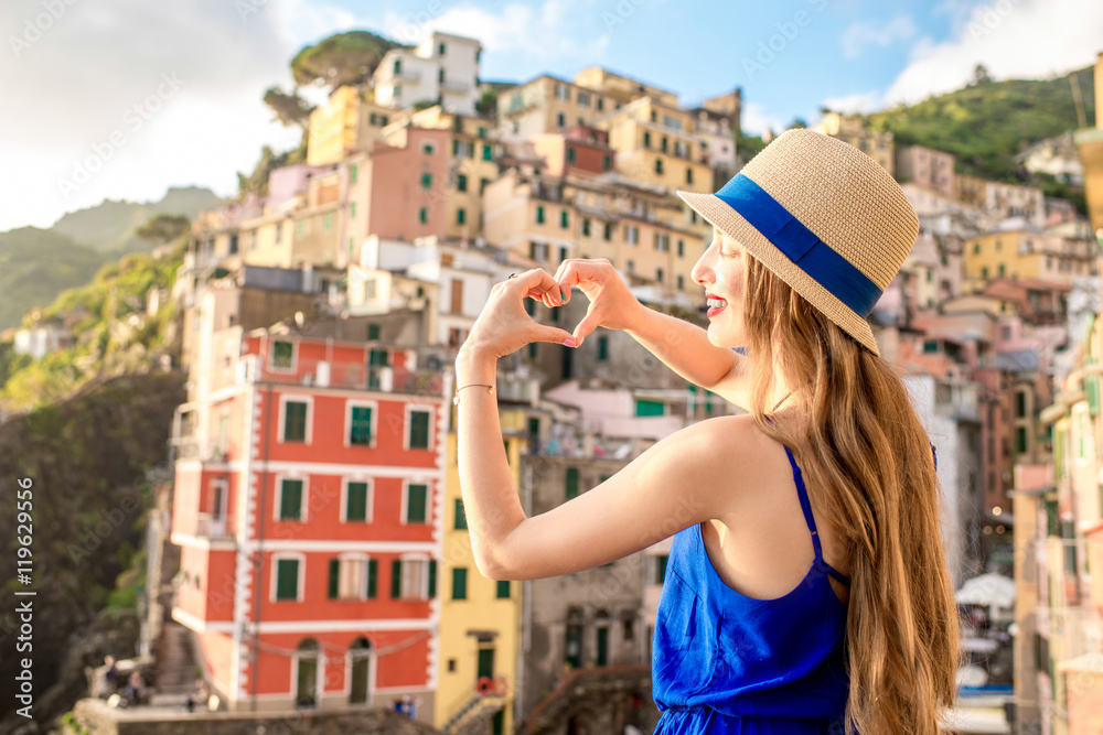 Young female traveler in blue dress making with hands heart shape on the old coastal town backgound 