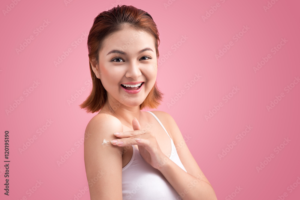 Woman use body lotion on arms and touching her skin on pink back