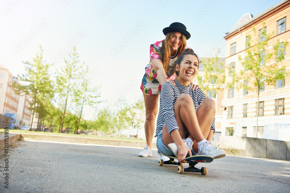 快乐的年轻女子推着朋友玩滑板