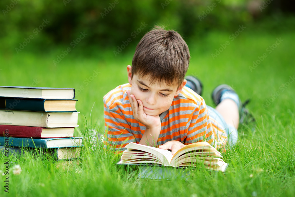 seven years old child reading a book lying on the grass