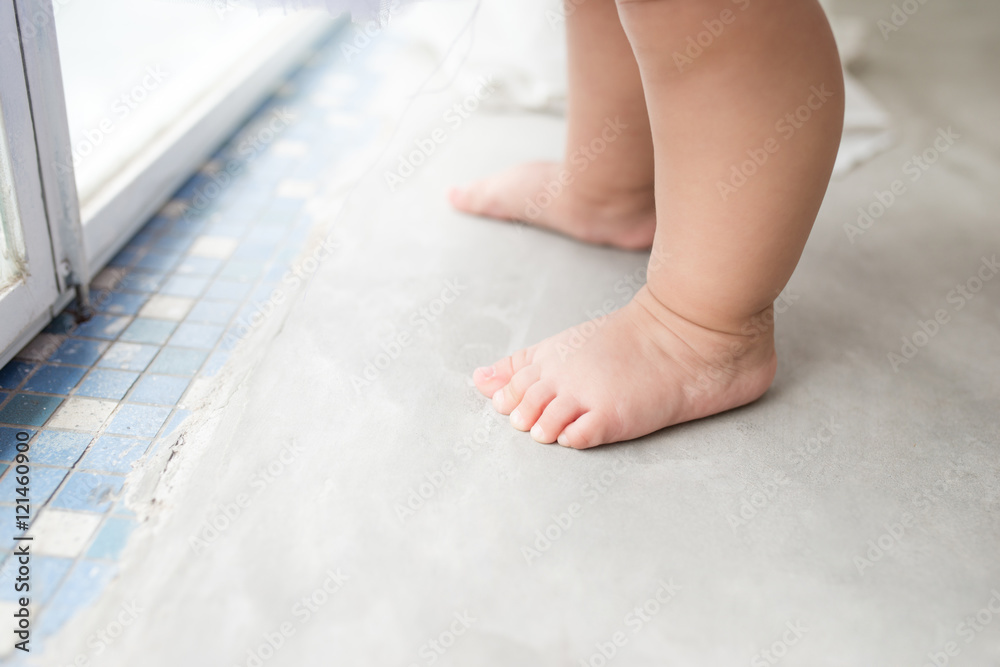 Little asian baby girl at home in white room stands near window.