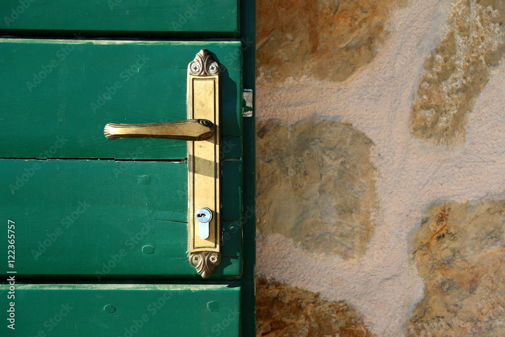 Traditional Dalmatian building exterior with stone wall and green wooden doors. Door handle close-up