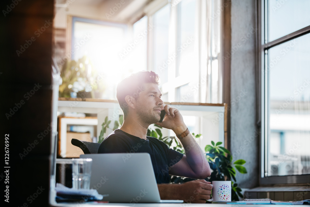 Businessman at his desk talking on mobile phone