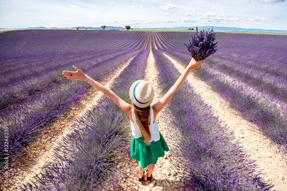 Young woman with raised hands holding lavender bouquet standing on the lavender field in Provence