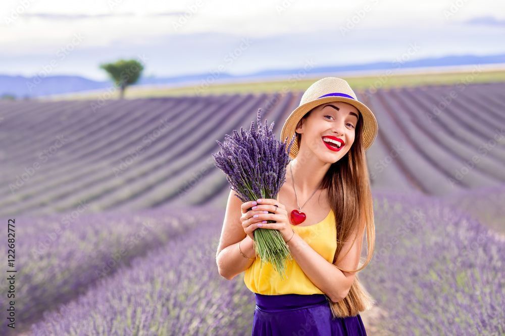 年轻漂亮的女人穿着紫色长裙，拿着薰衣草花束站在薰衣草地上