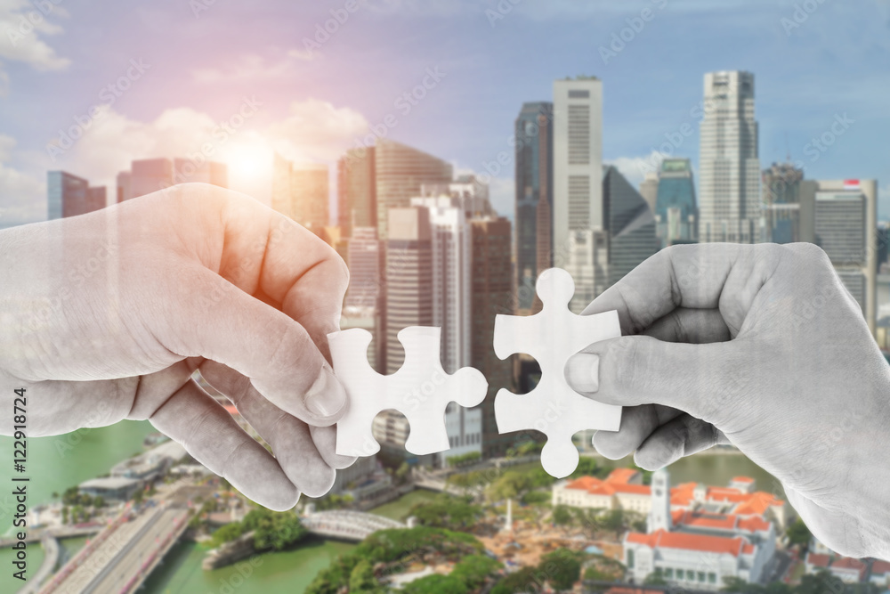 Hands putting partnership puzzle pieces together on skyscraper 