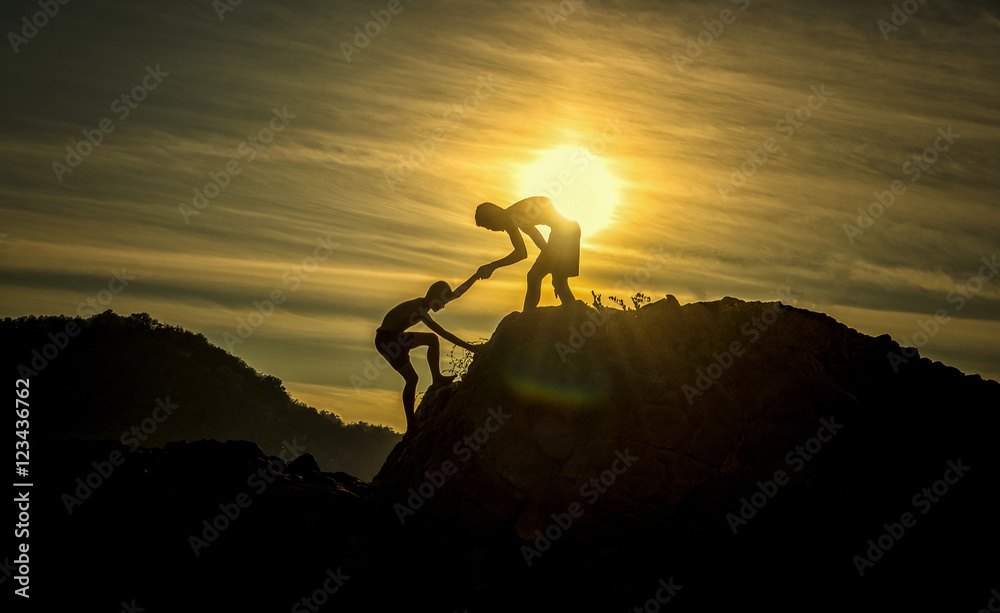 两名登山男孩之间的援助之手剪影