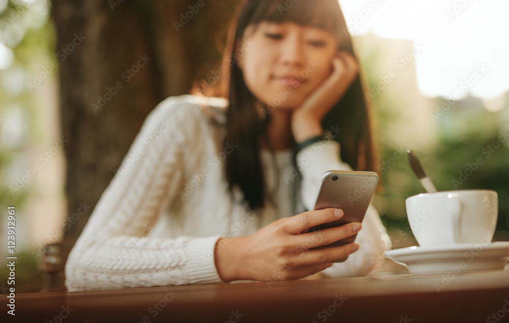 Young chinese woman using mobile phone at outdoor cafe